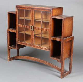 An Art Deco oak display cabinet fitted a shelf enclosed by panelled doors, flanked by niches, raised on square tapered supports with H framed stretcher 107cm x 117cm x 30cm