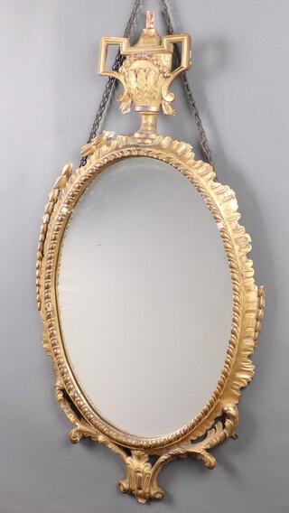 A 19th Century oval bevelled plate wall mirror contained in a carved gilt wood and plaster frame surmounted by an urn 102cm h x 52cm w 
