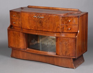 Stonehill Furniture, a 1960's walnut finished cocktail cabinet, the centre section with cocktail unit and Birdseye maple panelling, flanked by 2 short drawers, the base enclosed by glazed sliding panelled doors flanked by cupboards, raised on an outswept base 92cm h x 136cm w x 46cm d 
