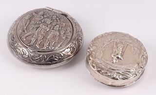 An embossed white metal circular box, the lid decorated figures 4cm and 1 other decorated a figure on a swing 3cm 