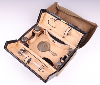 A 6 piece travelling vanity set comprising silver backed hand mirror with monogram and engine turned decoration 13cm Birmingham 1913, pin jar with silver lid and 4 small glass jars with silver lids London 1913, all contained in a leather case by Edwards and Sons of Regent Street (formerly the property of The Countess of Buxton) 
