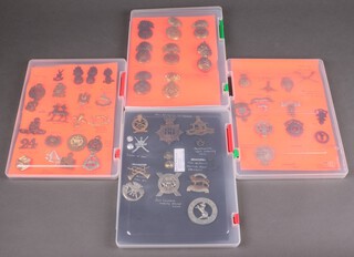 A collection of various re-strike military cap badges contained in four shallow cases