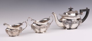 An Edwardian oval embossed silver bachelor's tea service comprising teapot with wooden handle, twin handled sugar bowl and milk jug, Birmingham 1906 by Williams, gross weight 509 grams 