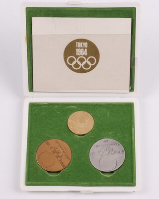 Tokyo Olympics 1964, a commemorative set containing 3 "medals" of 18ct gold 7.23 grams, 925 silver 18.55 grams and a bronze medal, contained in a fitted green plush case with white plastic exterior with Tokyo 1964 logo, complete with presentation leaflet 