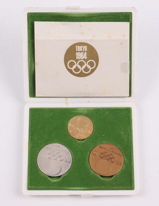 Tokyo Olympics 1964, a commemorative set containing 3 "medals" of 18ct gold 7.23 grams, 925 silver 18.55 grams and a bronze medal, contained in a fitted green plush case with white plastic exterior with Tokyo 1964 logo, complete with presentation leaflet 