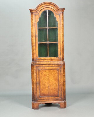 A 1930's Queen Anne style walnut corner cabinet with arched top, fitted shelves enclosed by astragal glazed panelled doors, the base enclosed by panelled doors, raised on bracket feet 177cm h x 40cm w x 58cm d 