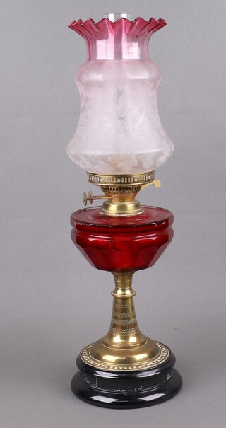 A Victorian faceted red glass oil lamp reservoir on an embossed brass base with socle ceramic base, associated red etched glass shade and chimney, fittings marked Duplex 59cm  