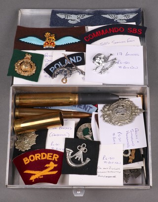 A collection of various re-strike cap badges, shoulder titles and cannon shells contained in an aluminium box with hinged lid