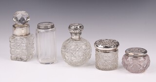 An Edwardian globular cut glass scent bottle complete with stopper and embossed silver lid, Birmingham 1901, 9cm (lid dented), a panel cut pin jar with silver lid 8cm (lid dented), a square cut glass perfume bottle with silver collar 10cm (chips to rim) and 2 small circular cut glass dressing table jars with silver lids 