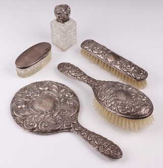 A filled silver and embossed 3 piece silver backed dressing table set with hand mirror (a/f), hair brush and clothes brush Birmingham 1959 by W I Broadway & Co., together with an oval cut glass dressing table jar with silver lid (dents to lid) and a pair of cut glass scent bottles with silver lids (dents to kids) 