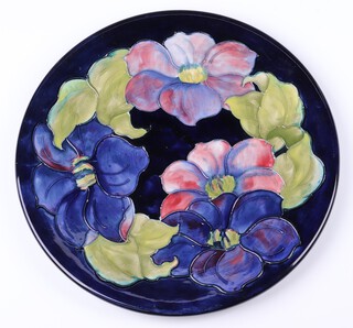 A Moorcroft blue glazed clematis pattern platter, the reverse impressed Moorcroft and with paper label Potter To The Queen, 31cm diam. 