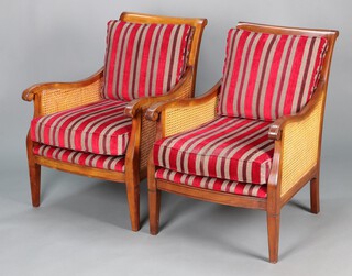 A pair of "cherry" bergere style armchairs with double cane panels to the sides and single to the back, complete with cushions in striped material 87cm h x 63cm w x 64cm d 