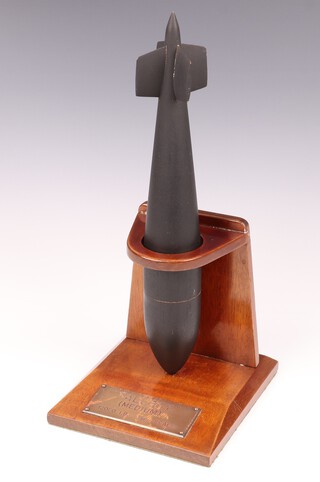 A wooden model of Tallboy (Medium) Bomb  32cm, raised on a mahogany stand with brass plaque marked Tallboy (Medium) 12,000 LB. 1/20 scale.  The Tallboy was the first bomb Wallis designed after the success of the bouncing bomb. The bomb was so large, there were no aircraft capable of lifting it to its optimal altitude but it could be dropped from a lower height and would enter the earth at near supersonic speed, penetrating to a depth of up to 20m before exploding. The Tallboy was used on strategic German targets such as V-2 rocket launch sites, the V-3 supergun bunker, submarine pens and the battleship Tirpitz, as well as large civil constructions such as viaducts and bridges