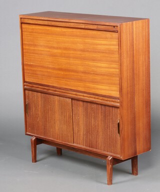 A mid-century teak bureau the fall front revealing a fitted interior with pigeon holes, above a cupboard enclosed by sliding panelled doors 102cm h x 91cm w x 27cm d 