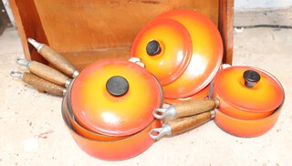 Five Le Creuset burnt orange saucepans and covers together with a saucepan stand 