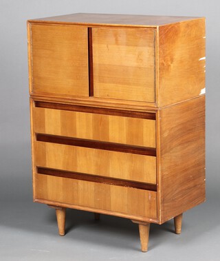 Merrydew, a mid-century teak finished tallboy, the upper section with cupboard enclosed by panelled doors, the base fitted 3 long drawers, raised on turned supports 112cm h x 76cm w x 46cm d  (veneers missing in places) 