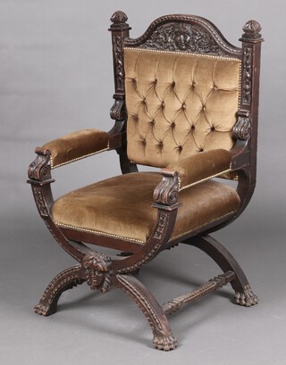 A Victorian carved oak Italian style open arm chair, the crest carved a portrait mask, upholstered in brown buttoned material, raised on an X framed stretcher 