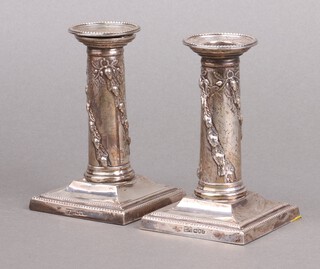 A pair of embossed silver candlesticks with detachable sconces, decorated acorn swags on square bases, London 1902 by Walker & Hall, 12cm, inscribed to base