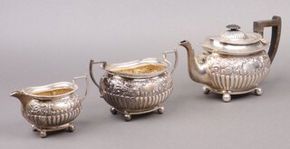 An Edwardian embossed silver 3 piece tea service comprising teapot, twin handled sugar bowl and cream jug, all on bun feet, Sheffield 1903 by Martin Hall & Company, 1163g