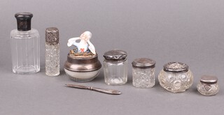 A faceted glass scent bottle with silver top (dented), a cut glass scent bottle with embossed silver top, 2 cut glass dressing table jars with silver lids (dents), 2 jars with silver lids (dents) and a cut glass and silver mounted powder puff 