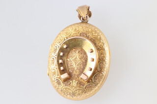 A gold testing as 9ct pendant locket with horseshoe and engraved decoration of foliate scrollwork and a wolf, 4.5cm, 18g gross (including 2 internal pins) 