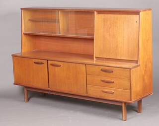 A mid-century teak sideboard, the raised back fitted a cocktail unit, display cabinet enclosed by glazed panelled doors above a recess, the base fitted a cupboard enclosed by panelled doors, flanked by 3 drawers 123cm h x 184cm w x 46cm d (veneers missing in places)