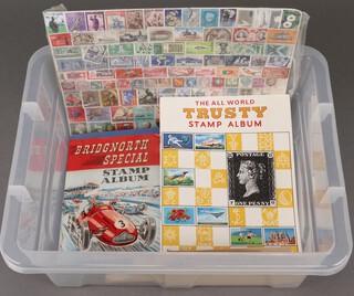 An All The World Trusty stamp album containing a collection of used stamps, an Improved stamp album and a collection of of loose stamps, all contained in a plastic box 