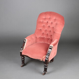 A Victorian armchair upholstered in pink buttoned material and ebonised show frame, raised on turned supports 