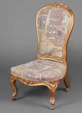 A Victorian gilt painted nursing chair upholstered in green and gilt fabric, seat of serpentine outline, raised on cabriole supports 