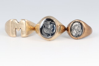 A 9ct gold initial "M" ring, size N, 6.8g, a 9ct hardstone set signet ring (cut) and a yellow metal ditto, size N, 