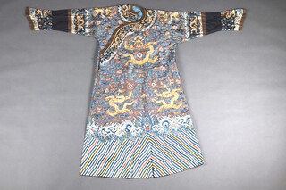 A Chinese 19th Century embroidered blue silk Ch'i-fu "Dragon" robe, finely worked in gold couched thread, Peking knot and satin stitch with five-clawed writhing dragons pursuing a flaming pearl, amongst clouds, all above foaming waves and a broad lishui band at the hem, with dragon embroidered cuffs