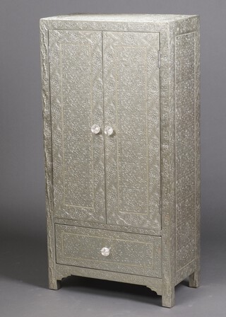 An Indian embossed metal cabinet with floral decoration,  enclosed by panelled doors, the base fitted a drawer 130cm h x 64cm wide x 35cm d  