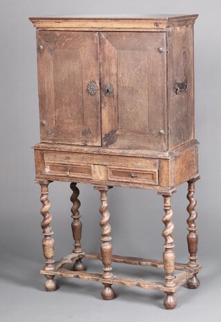 A 17th Century style oak cabinet on stand, the upper section with moulded cornice and iron carrying handles to the sides, interior with glazed base and back fitted a shelf, the base fitted a drawer with geometric mouldings, raised on a spiral turned column, the base with wavy stretcher 140cm h x 74cm w x 38cm d 
