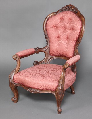 A Victorian carved walnut show frame open arm chair upholstered in pink buttoned material, raised on cabriole supports 
