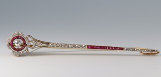 An early 20th Century Art Deco platinum and gold, diamond and ruby set surete pin/brooch, the finial with a central old cut diamond approx 0.25ct surrounded by rubies and diamonds, the narrow tapering stem set rubies between 2 lines of single diamonds, 9cm long  