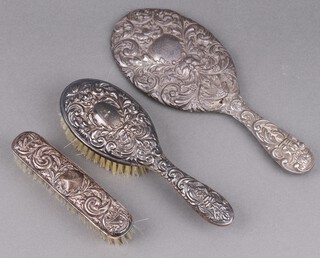 An Edwardian silver backed hand mirror with embossed decoration, Chester 1903 (some holes) together with an embossed silver backed hair brush and clothes brush Birmingham 1961  