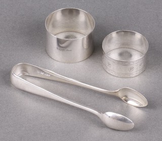 An Edwardian plain silver napkin ring Birmingham 1908, an engraved silver napkin ring Birmingham 1879 and a pair of Old English pattern silver sugar tongs Sheffield 1934, 102g  