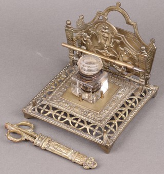 A Victorian square cut glass inkwell with brass pierced standish incorporating a letter rack and with dip pen and scissors (chips to inkwell)