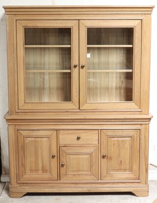 A light oak dresser/display cabinet, the upper section with moulded cornice, the interior fitted shelves enclosed by glazed panelled doors, the base fitted a drawer above cupboard, flanked by cupboards on bracket feet 197cm h x 150cm w x 48cm d  