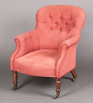 A Victorian armchair upholstered in pink buttoned material, raised on turned supports 