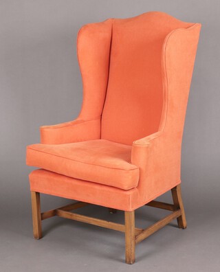 A Georgian style mahogany winged armchair, upholstered in orange material, raised on square tapered supports with H framed stretcher 