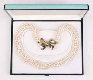 A 7 string multi row necklace of seed pearls with central bow shaped pendant marked 750, boxed 