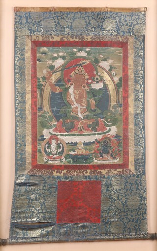 A Tibetan Thanka, early 20th century gouache on silk, the central deity Manhushri in a seated lotus pose upon a throne, surrounded by two other deities, 97cm x 55cm, within a gilt frame.	