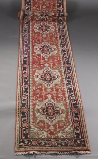 An orange, black and white ground Persian runner with 9 stylised medallions within a multi row border 602cm x 77cm 
